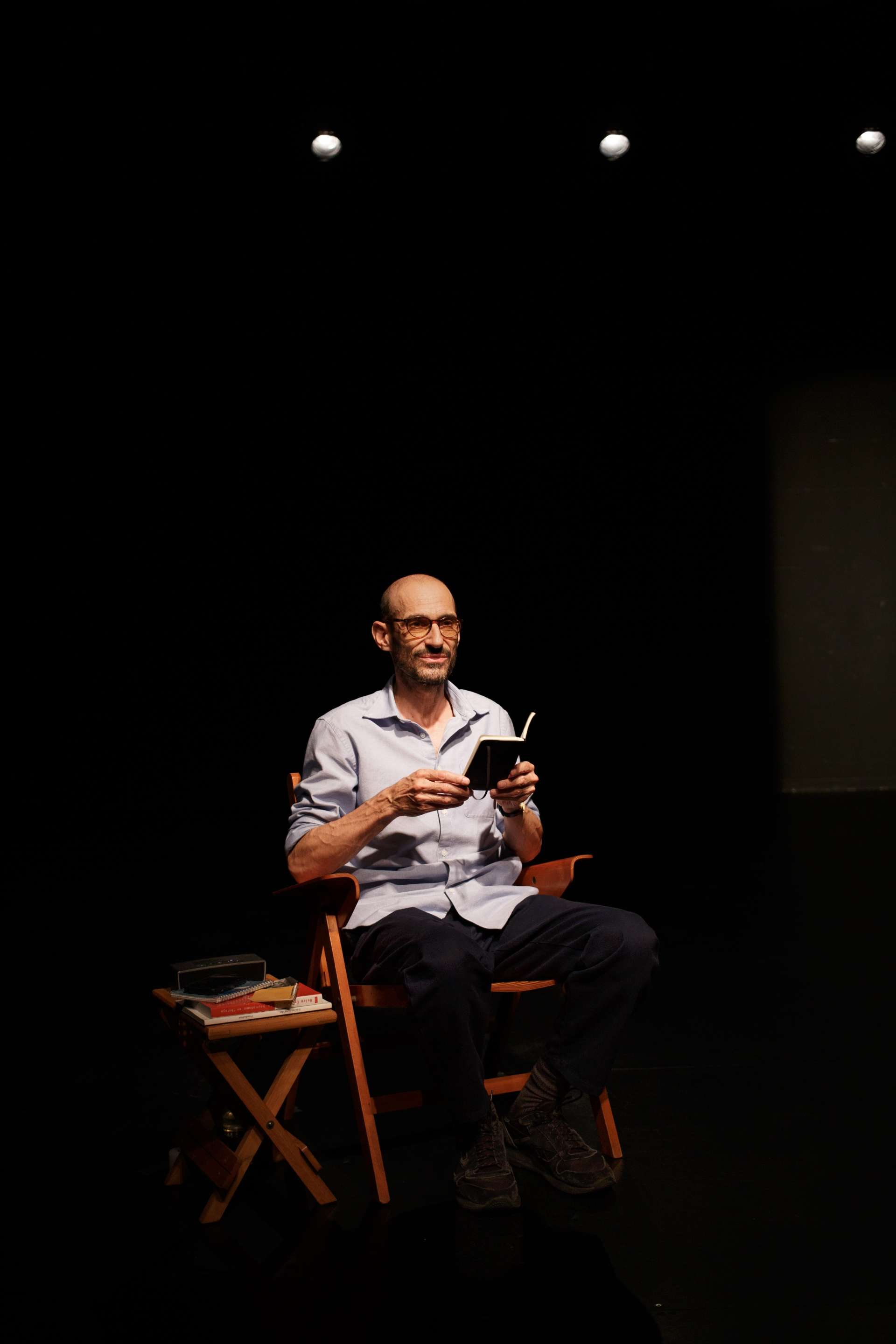 eric feldman assis sur une chaise en bois lisant un livre sur scène