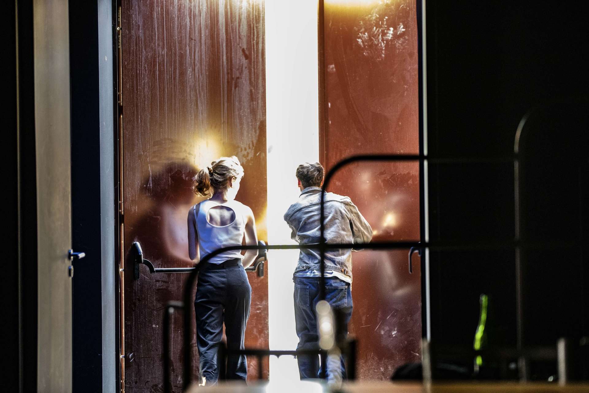 2 personnes de dos pousse une porte hautele lumière entre par l'entrebaillement