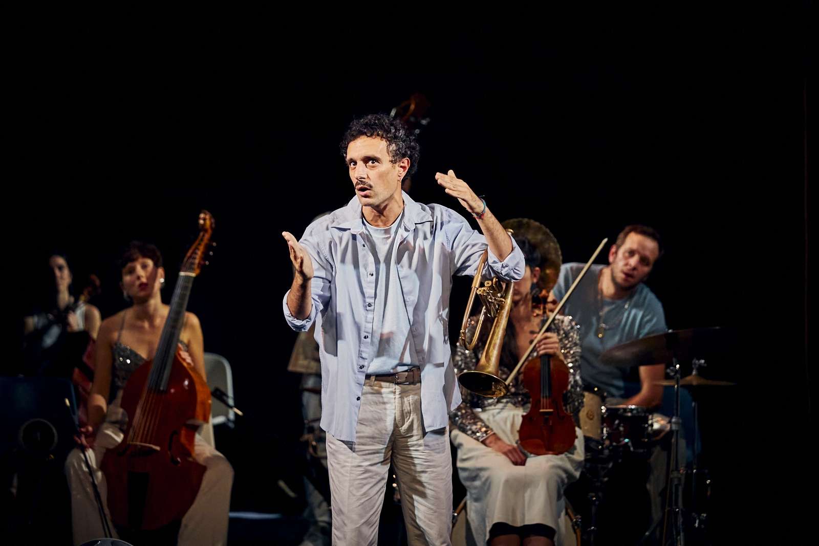 musiciens sur scène et au premier un homme debout semble indiquer quelque chose à l'oral