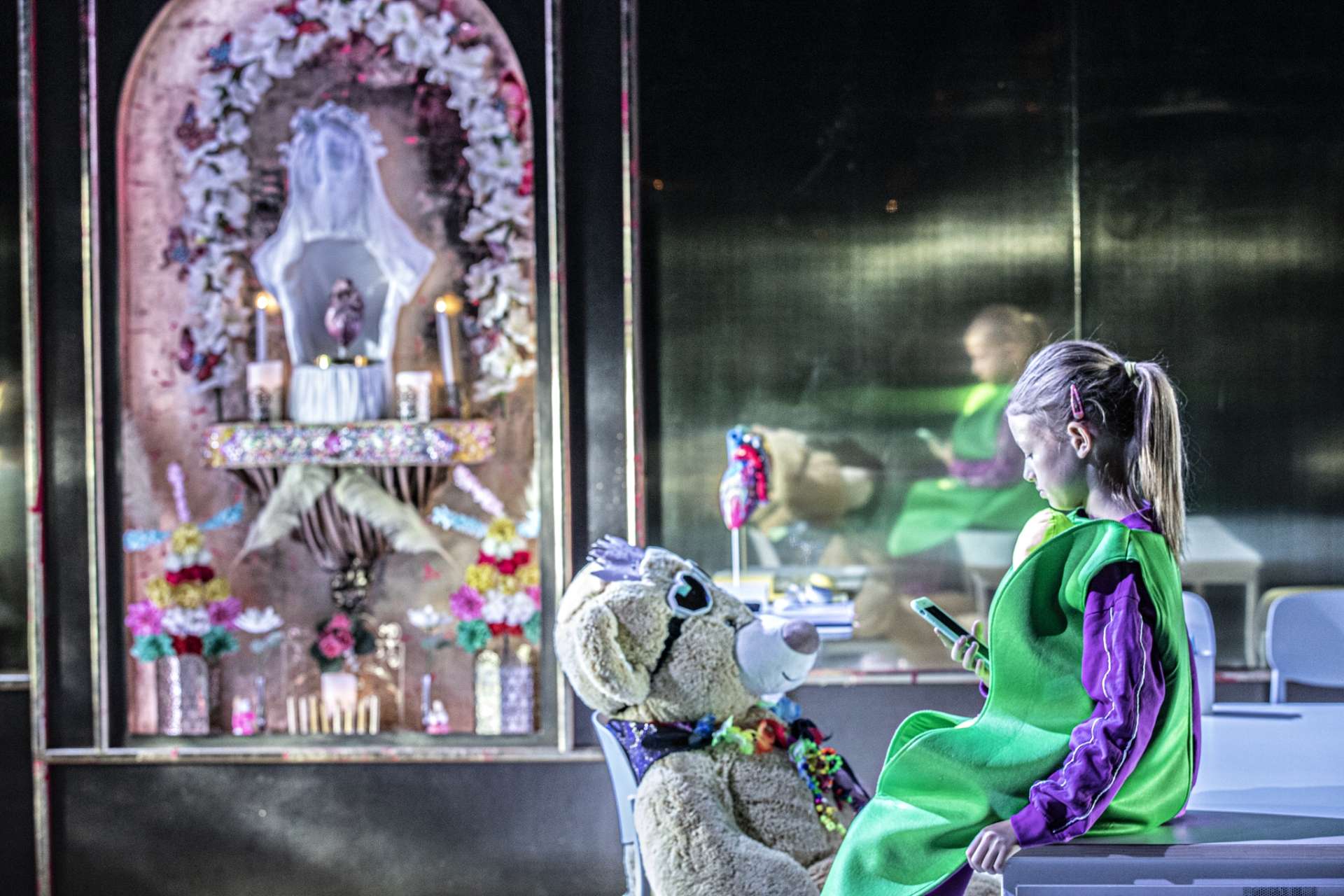 dans Valentina de Caroline Guiela Nguyen une enfant déguisée en petit pois assise sur une table avec un gros nounours avec son reflet au loin par Jean-Louis Fernandez