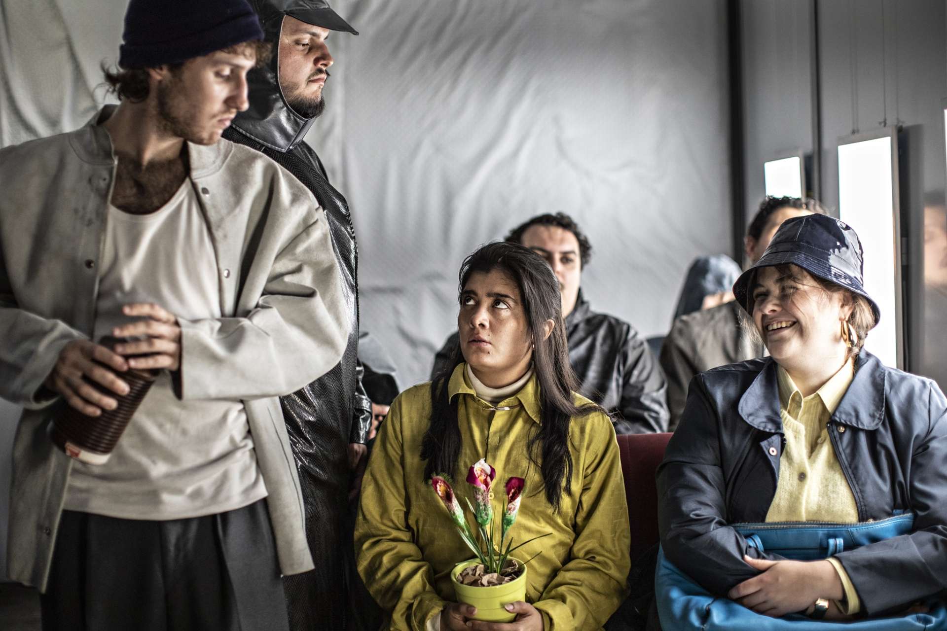 Un groupe de personnes dans un bus. Parmi eux, deux hommes et deux femmes se regardent. L'une des femmes sourit à pleines dents, l'autre semble inquiète.
