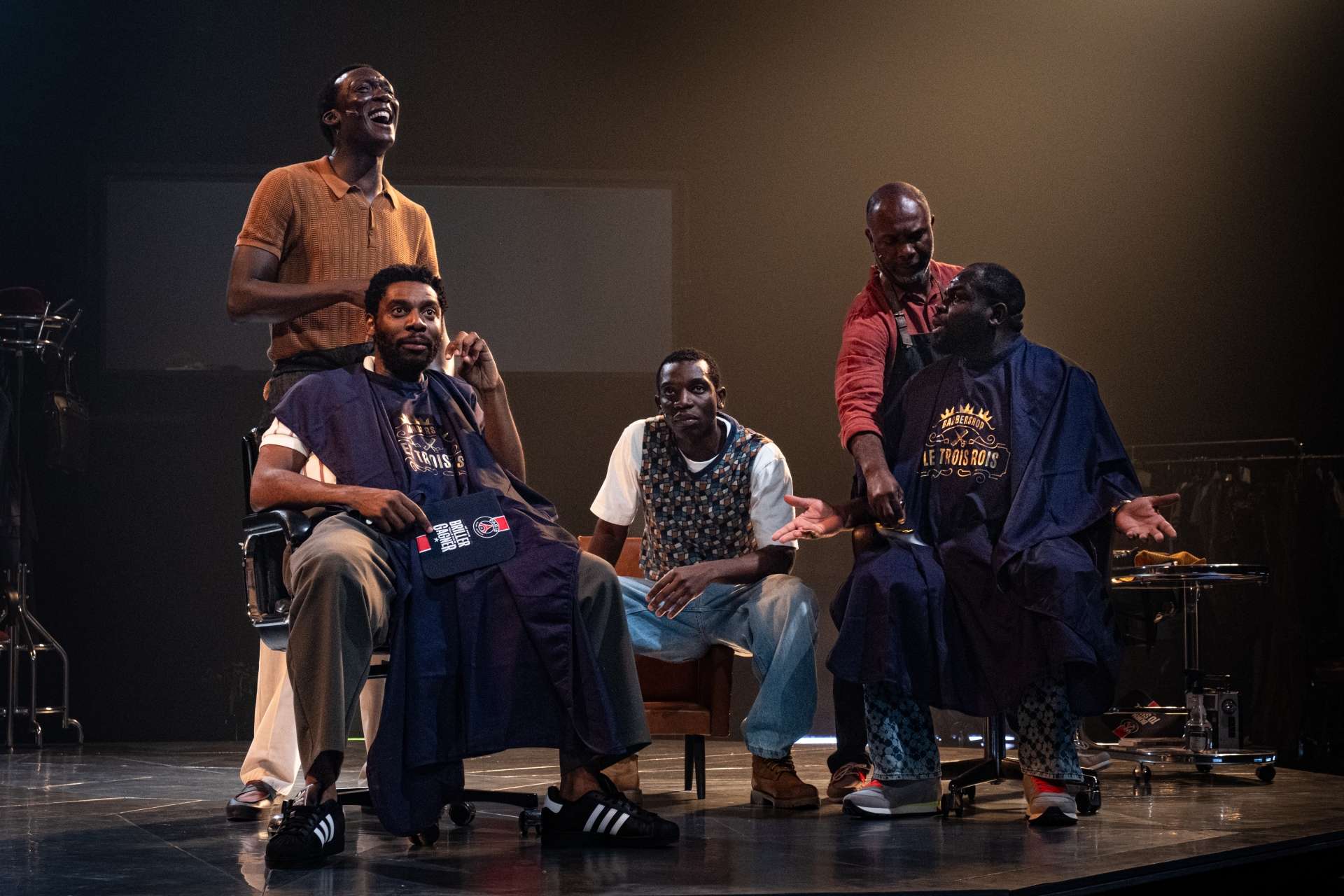 Barber Shop Chronicles © Stef Stessel 5 hommes noirs chez le barbier ambance joyeuse et sourire aux levres